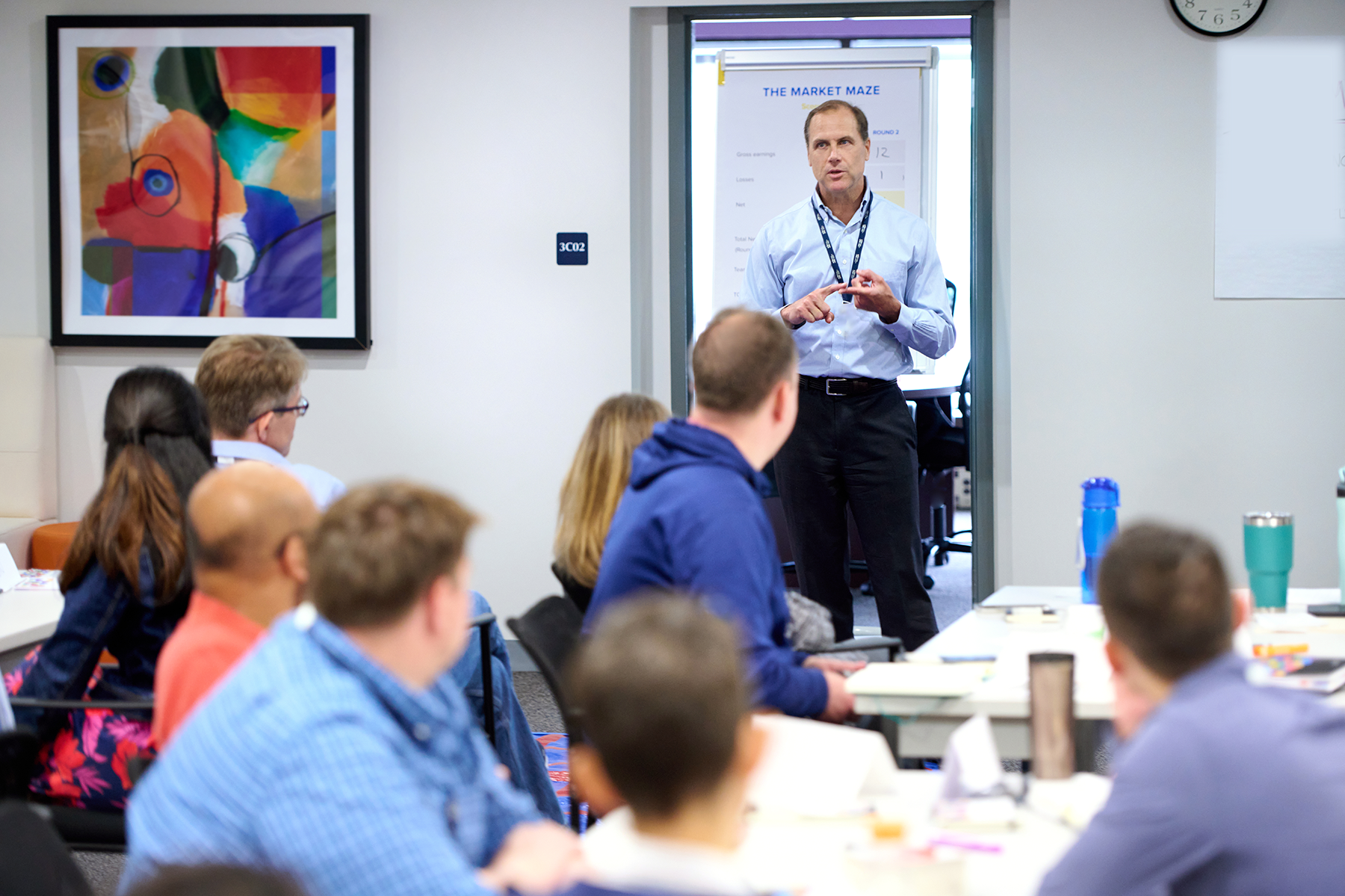 A facilitator leads a workshop discussion with engaged participants seated around tables in a modern classroom setting.
